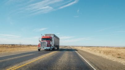 An 18-wheeler driving down a deserted highway, meant to represent the article "The Liability of Big Trucks" by MMRBH Law Office.