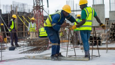 construction workers are seen wearing hard hats and hi-vis vests, doing various tasks at the scene of a construction site. This is meant to serve as a header image for the article "5 steps to take after a workplace injury" by MMRBH Law Office.