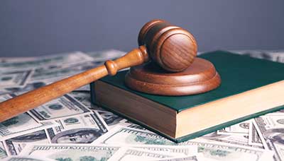 A wooden gavel laying atop a book, with a spread of money below. This photo serves as a header image for the article "3 Key Differences Between Mass Tort and Class Action Cases" by MMRBH Law Office.